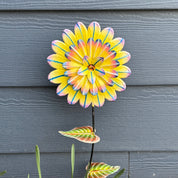 Colorful flower-shaped garden stake against blue siding.
