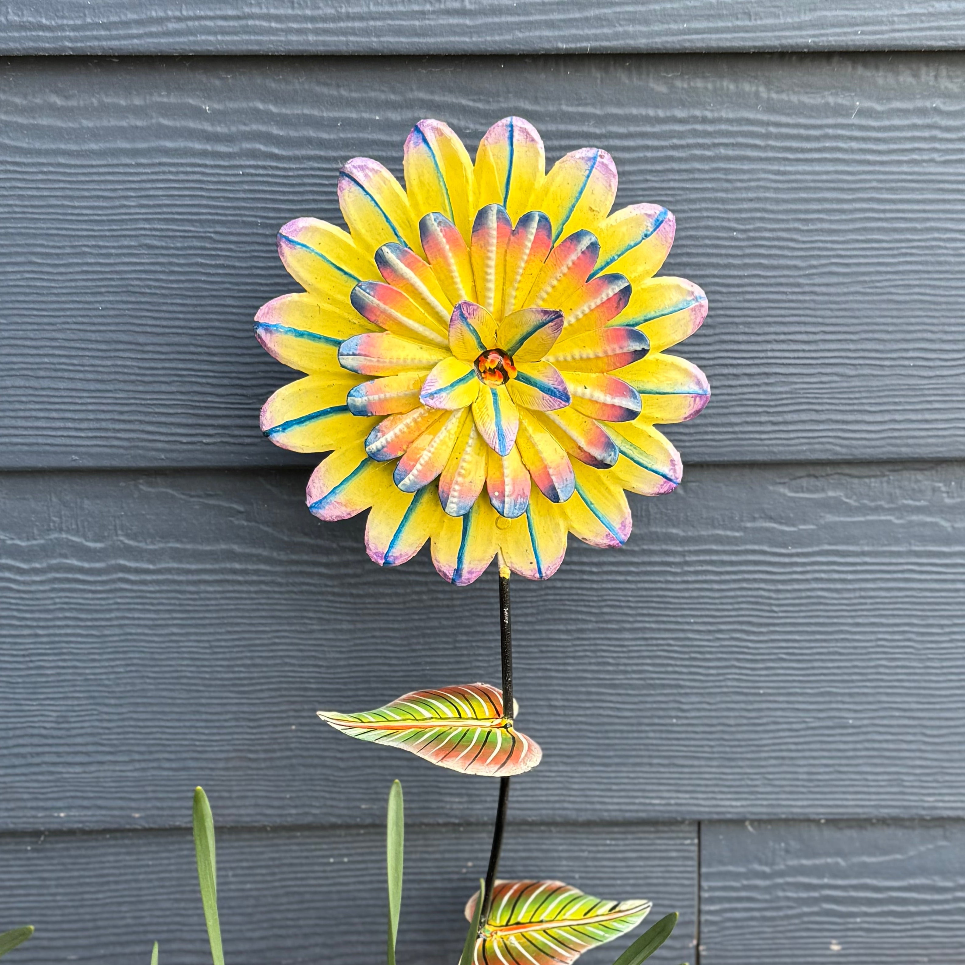 Colorful flower-shaped garden stake against blue siding.