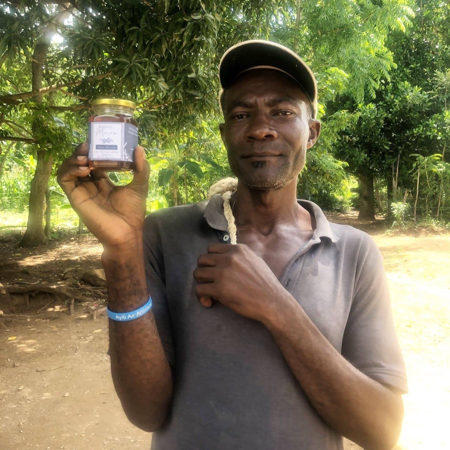 Man holding a jar of Haitian honey outdoors with greenery in the background