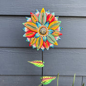 Colorful flower-shaped garden stake against blue siding.