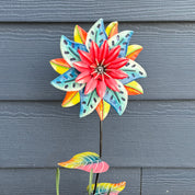 Colorful flower-shaped garden stake against blue siding.