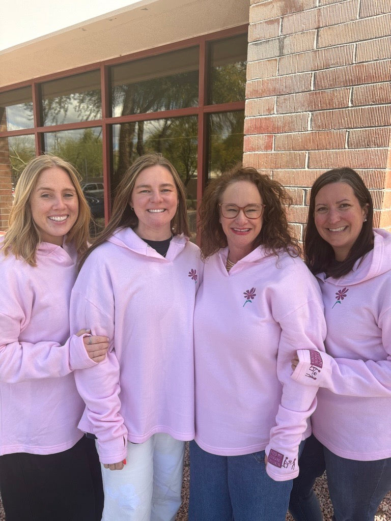 Four women wearing pink hoodies standing in front of a building.