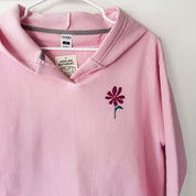 Pink hoodie with a flower design on a hanger against a white background