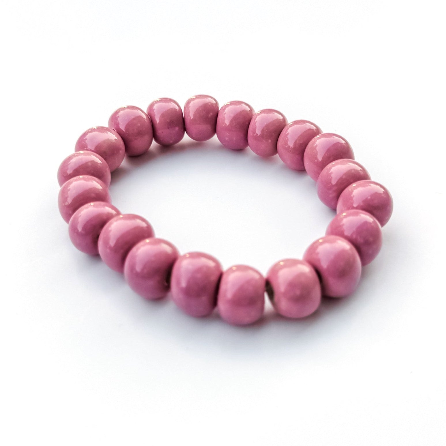 A pink beaded stretch bracelet made of smooth, glossy round clay beads, photographed on a clean white background.