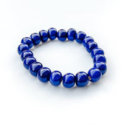 A beaded stretch bracelet made of glossy, deep blue round clay beads, photographed on a clean white background.