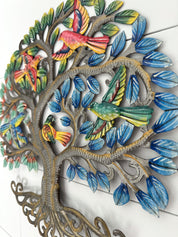A decorative metal wall art piece shaped like a tree with colorful birds perched among blue leaves, shown against a white paneled wall.