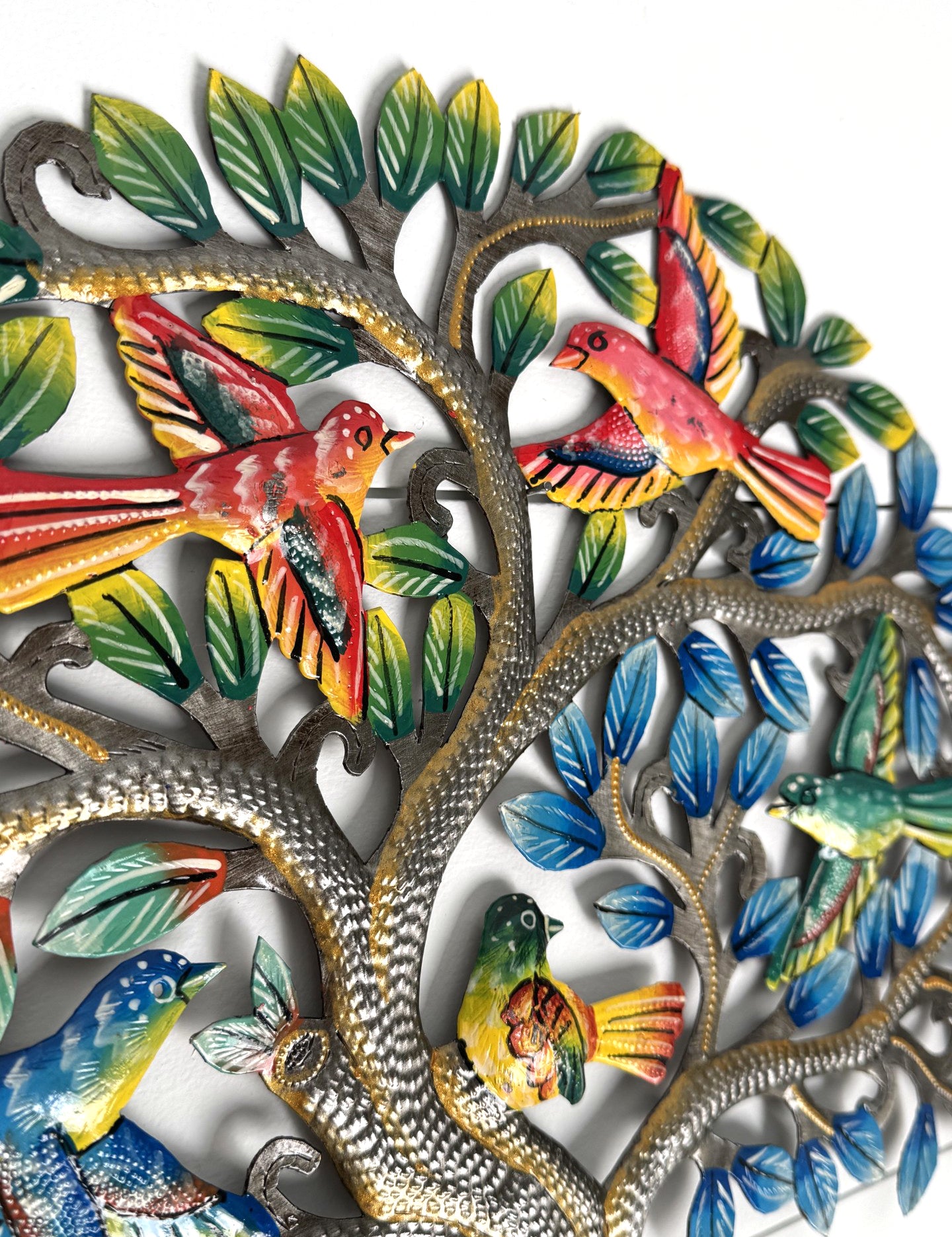 Colorful metal wall art featuring a tree with silver-toned branches, green and blue leaves, and several brightly colored birds in red, yellow, blue, and green, shown against a plain white background.