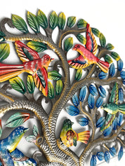 Colorful metal wall art featuring a tree with silver-toned branches, green and blue leaves, and several brightly colored birds in red, yellow, blue, and green, shown against a plain white background.