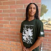 Person wearing a green t-shirt with a tree design and text, standing against a brick wall.