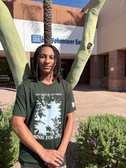 Person wearing a green t-shirt with a forest graphic and text, standing outside Feed My Starving Children.