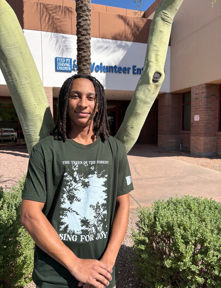 Person wearing a green t-shirt with a forest graphic and text, standing outside Feed My Starving Children.