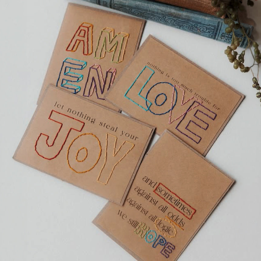 Four Kraft cards with embroidered text hand-stitched by artisans in Haiti.