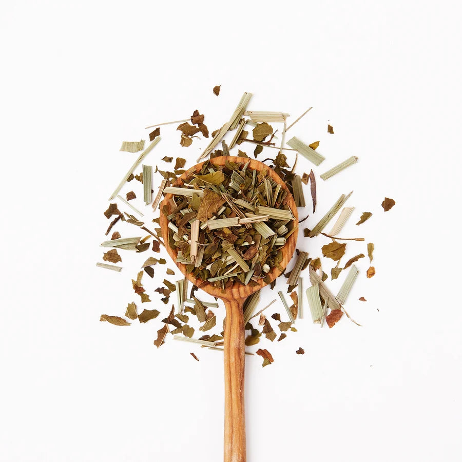 Wooden spoon filled with dried tea herbs on a white background